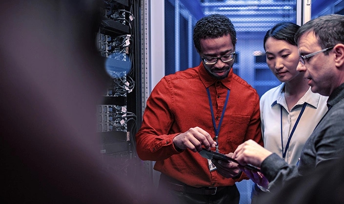 A team of professionals working together in a data center, examining equipment & cables of a server rack.