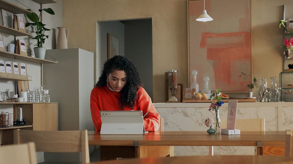 Woman working on a Lenovo tablet in a cozy, modern café, focused on producitivity tasks with pen.