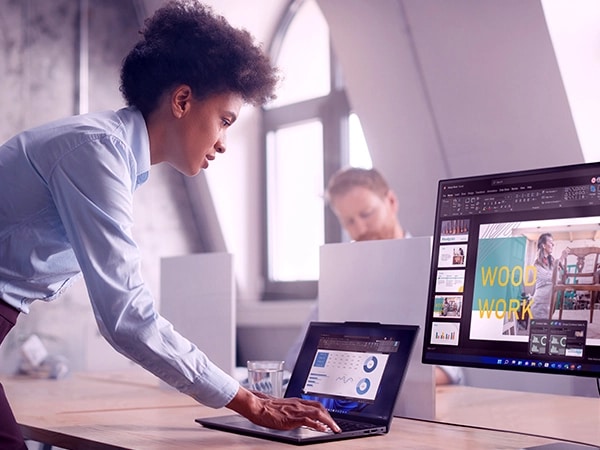 A person standing & leaning over a desk typing on a Lenovo ThinkPad X13 Gen 4 laptop that is connected to a monitor.