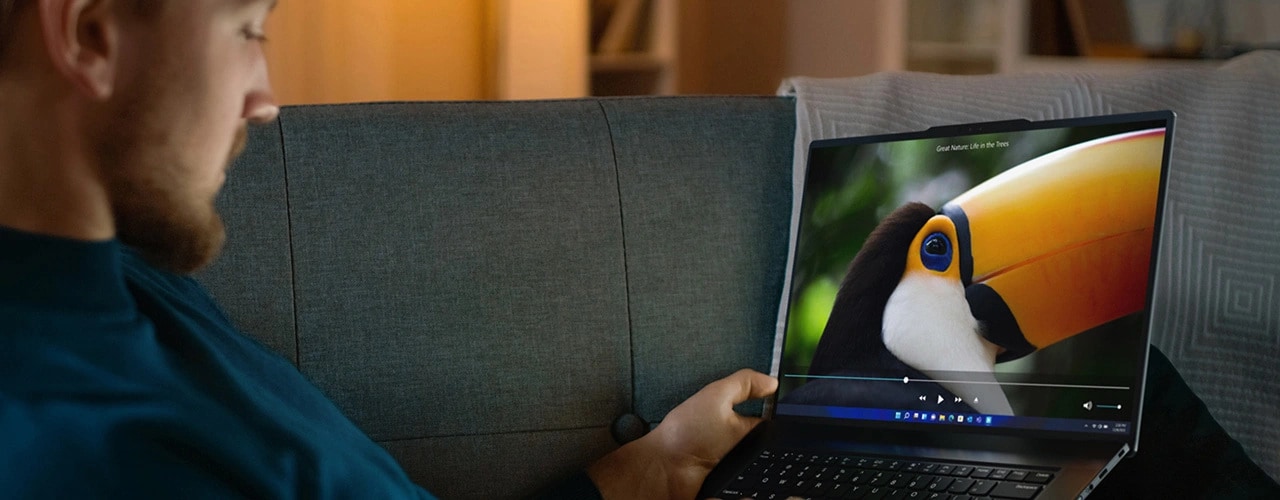 Ein Mann lehnt sich auf einer Couch zurück und schaut sich auf dem Lenovo ThinkPad Z16 Gen 2 Notebook ein Video an.