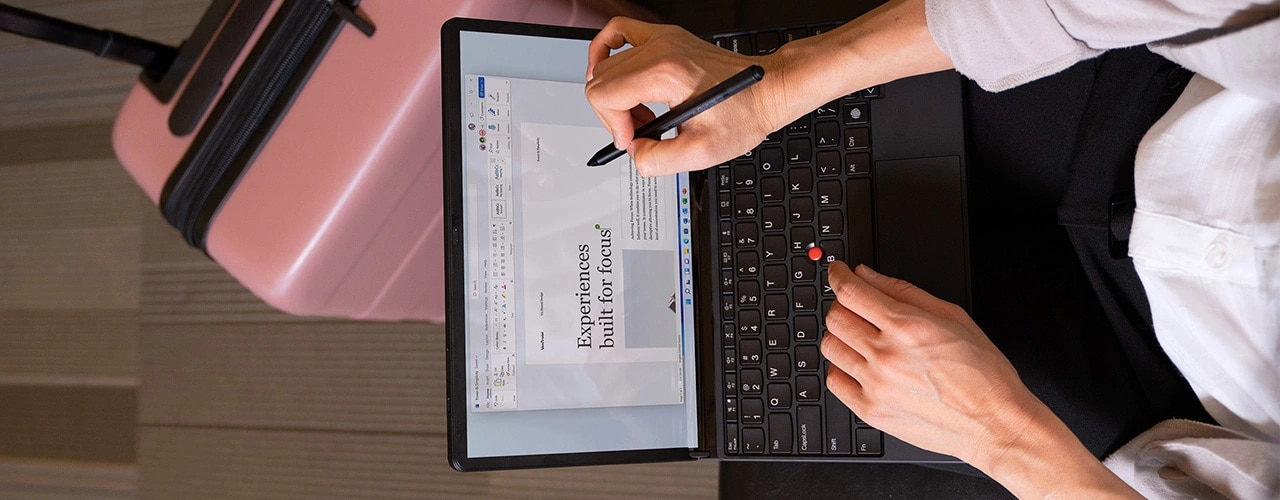 Vista dall'alto di una donna con il dispositivo Lenovo ThinkPad X1 Fold acceso, appoggiato sulle ginocchia e collegato alla tastiera con TrackPoint, che annota con una penna il documento Word nella schermata.
