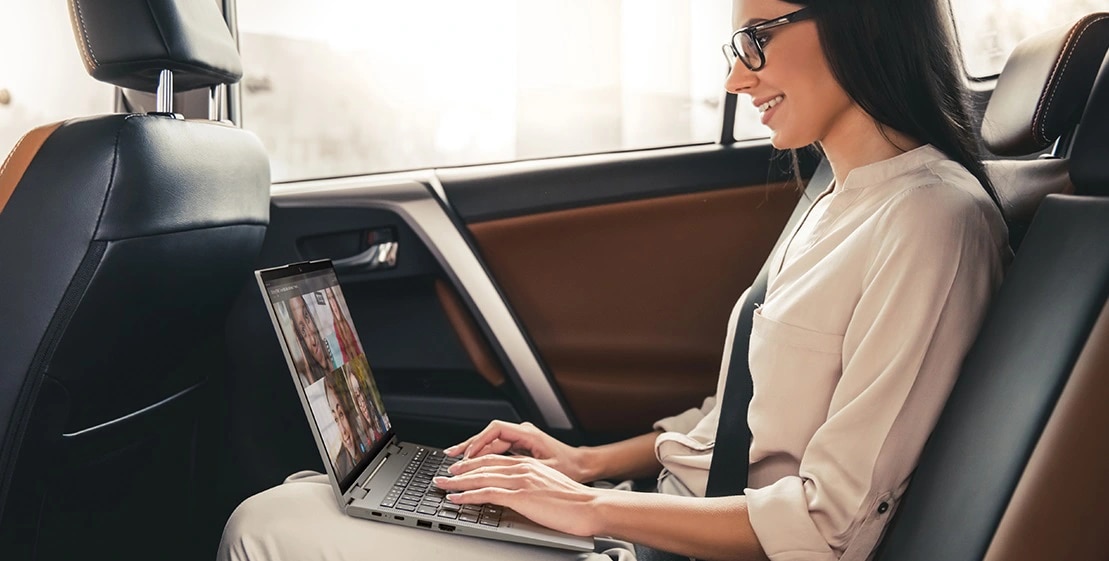 A woman in the backseat of a car with a video call on the Lenovo ThinkPad X1 Yoga Gen 8 2-in-1 laptop.
