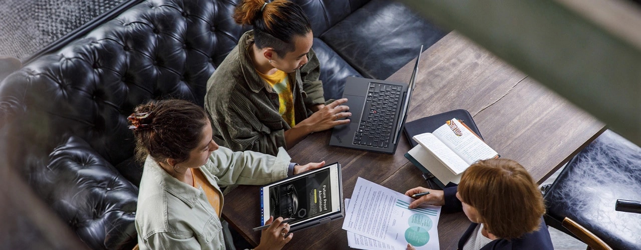 Obersicht auf drei Personen, die um einen Tisch sitzen und arbeiten. Zwei davon verwenden wandelbare Lenovo ThinkPad X1 2-in-1-Notebooks der 9. Generation, einer davon tippt und einer verwendet den mitgelieferten Lenovo Slim Pen.