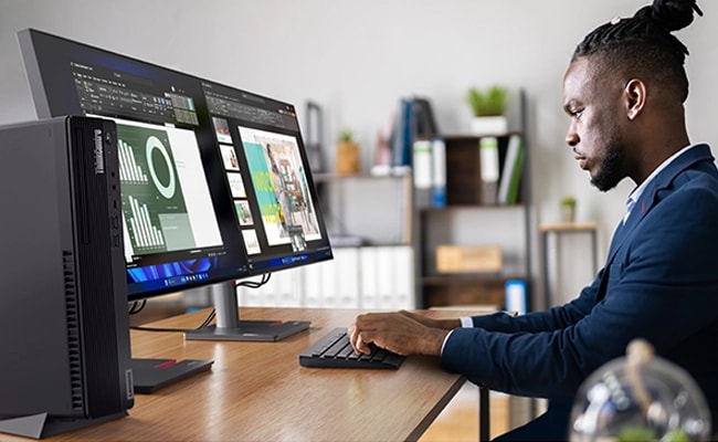 Ein junger Mann arbeitet an einer Power-Point-Präsentation auf einem superbreiten Monitor, wobei das Lenovo ThinkCentre 90s Gen 5 im Vordergrund steht.