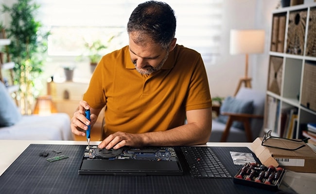 A man on a desk does maintenance on a laptop computer by himself.