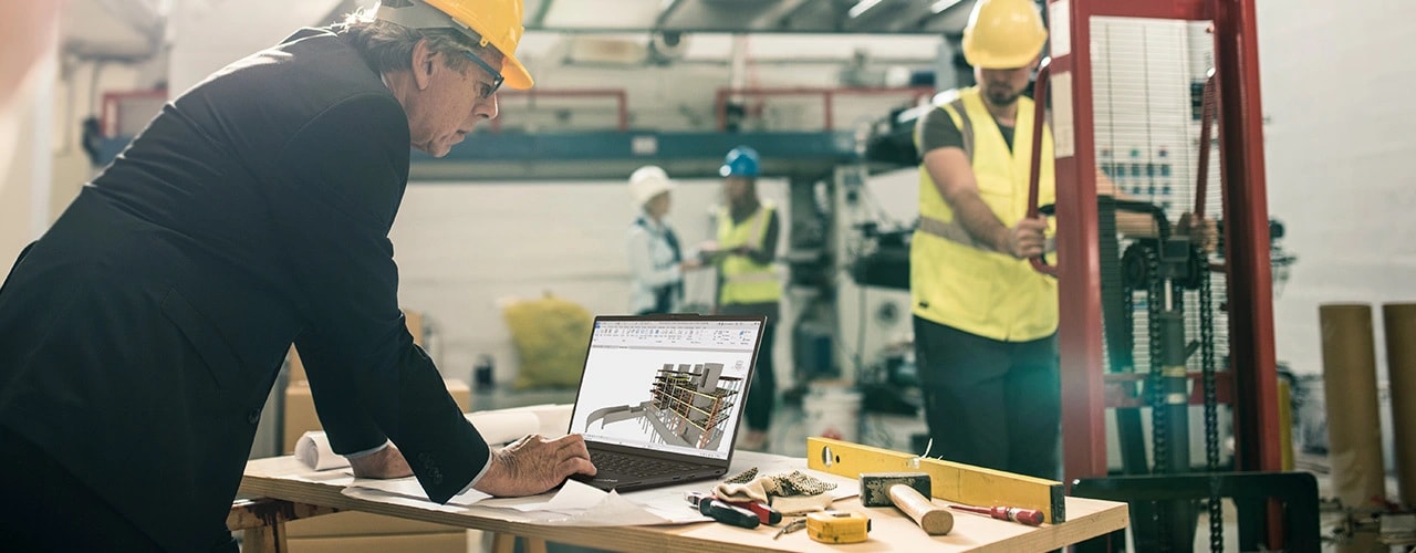 A person working on the Lenovo ThinkPad P14s Gen 5 (14 inch Intel) black laptop placed on a desk in an indoor construction setting with other workers & reviewing some data-centric technical drawings on the laptop.