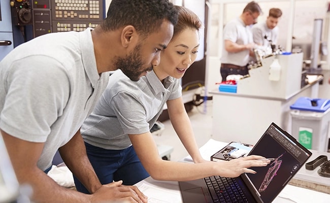 Two people working on a graphics app opened on the Lenovo ThinkPad P14s Gen 5 (14 inch Intel) black touchscreen laptop placed on a desk in a technical lab setting with some other people working in blur background.