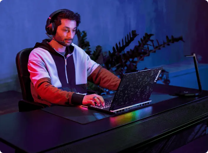 A person sitting in a darkened room, wearing Lenovo Legion gaming headphones and playing on a Lenovo Legion gaming laptop.