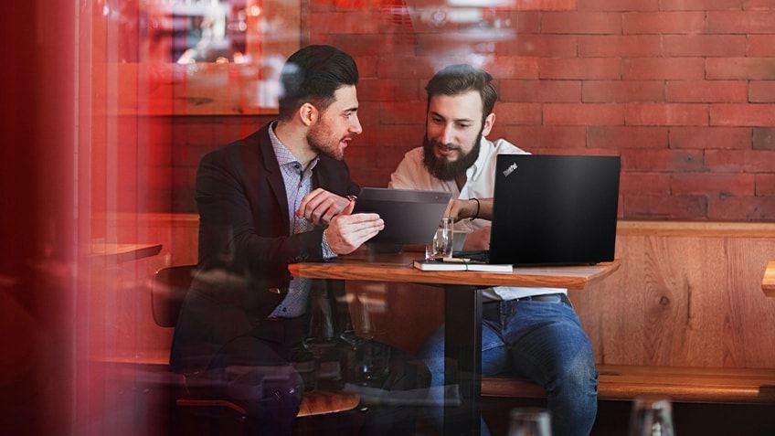 Four people meeting in an all-glass conference room with colleagues moving about around them.