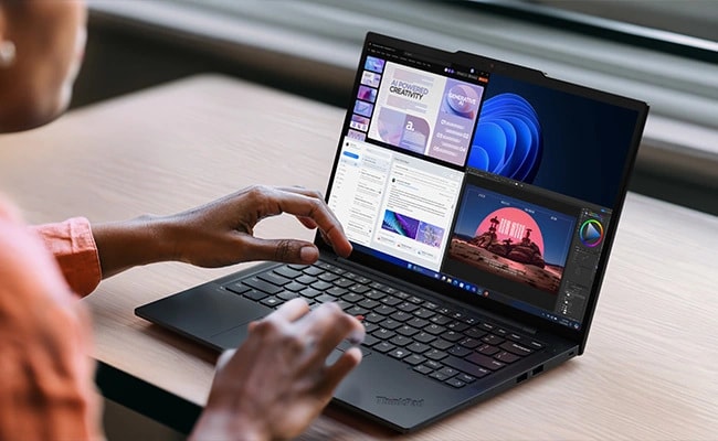 Eine Person, die mit dem Lenovo ThinkPad T14s Gen 6 (14'' AMD) Notebook arbeitet, das auf einem Schreibtisch mit mehreren geöffneten Anwendungen auf dem Bildschirm platziert ist und dessen KI-Effizienz für Multitasking und höhere Produktivität im Mittelpunkt steht.