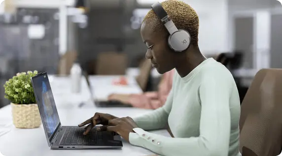 Profile view of a woman with headphones sitting at a desk, using a Lenovo laptop.