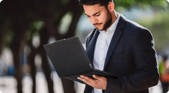 A man standing, holding a Lenovo ThinkPad laptop with one hand while using the keyboard/touchpad with his other hand.