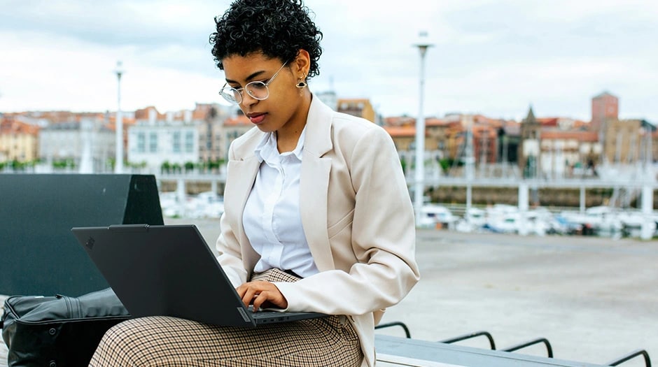 Una mujer en un entorno urbano al aire libre con un ThinkPad T14s de 6ª generación (14" Intel) en el regazo.