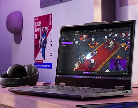 Lenovo LOQ Essential 15IRX11 gaming laptop on a desk with headset – right-front view, lid open, with a videogame screen on the display.