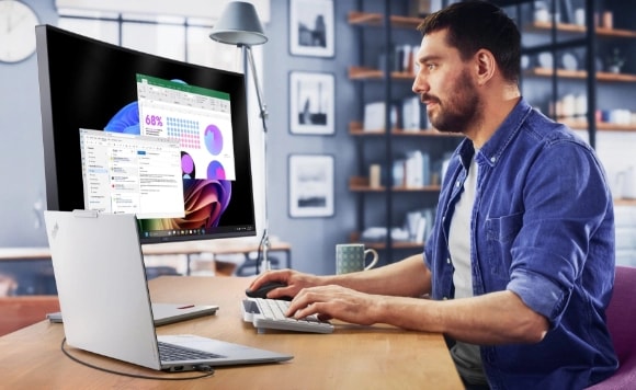 A man at a desk looks at a monitor as he types on a keyboard next to a Lenovo ThinkPad X9 laptop.