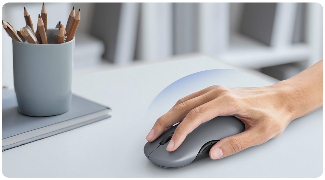 A hand grips a computer mouse on a wooden desk, indicating active computer use.