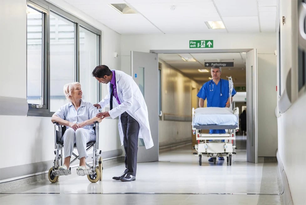 a hospital corridor with a doctor talking to a patient in a wheelchair
