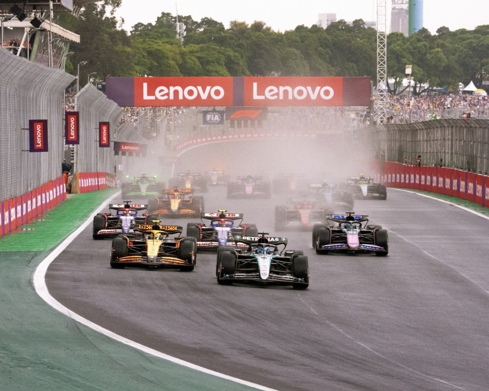 Escena dinámica de autos de Fórmula 1 en pista con humo y movimiento, ilustrando el caos y la emoción de la carrera patrocinada por Lenovo