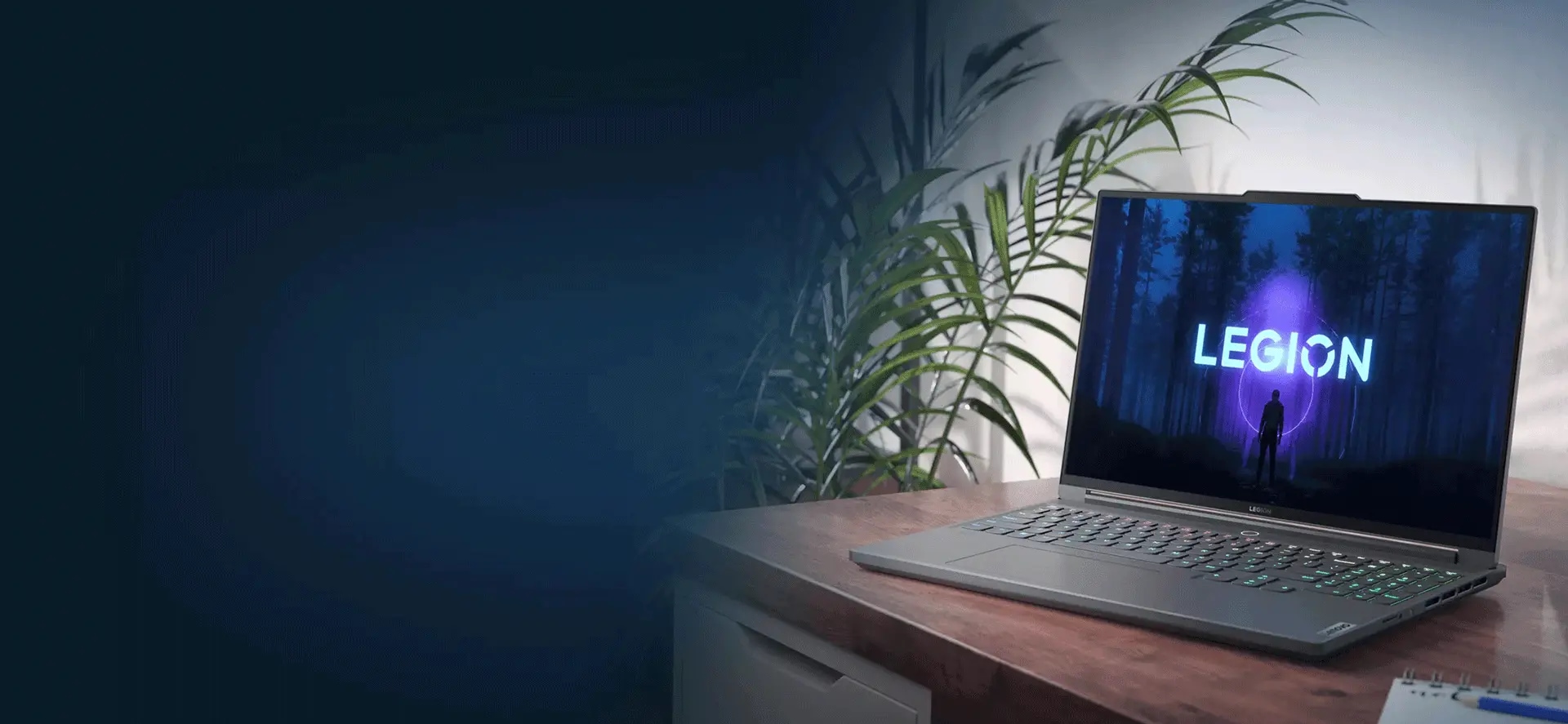 Bild snett från vänster av Lenovo Legion Slim 7 där den står på ett skrivbord med Legion-logotypen synlig på skärmen och med växter till vänster om skrivbordet i bakgrunden
