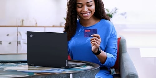 A smiling woman sits on a desk and looks for a credit card.