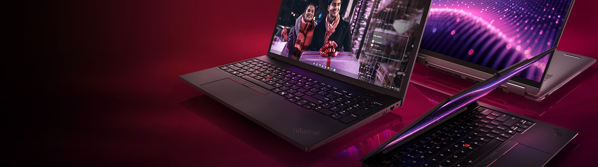 Three Lenovo laptops with a backlit keyboard and vibrant screen is displayed against a deep burgundy background.