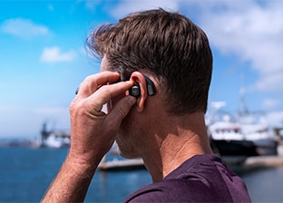A man wearing a JLab earbud while outdoors at a pier.