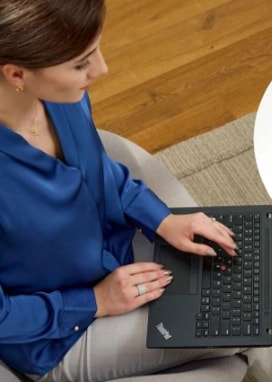 Seated at a small white coffee table, a professionally dressed woman looks over business reports on her ThinkPad laptop.