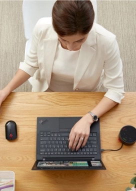 Vue d’en haut d’une femme assis à son bureau tout en buvant du café et en magasinant en ligne avec son portable Lenovo ThinkPad.