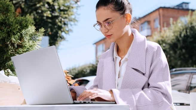 a woman sitting outside, working on a Lenovo laptop. The scene conveys a sense of tranquility and productivity.