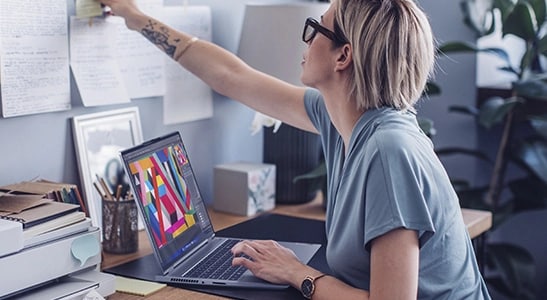 Two people talking to each other, one next to the other behind a table with a ThinkBook Yoga laptop on it