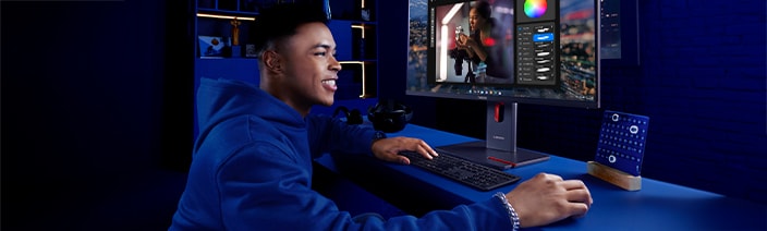 Person sitting at a desk using a Lenovo monitor to edit a photo with color adjustment tools, accompanied by a keyboard and mouse, in a dark blue workspace with modern décor.