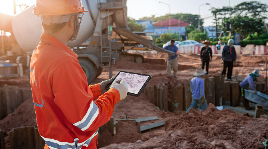 A worker at a busy construction site holds a Lenovo ThinkTab X11 tablet.