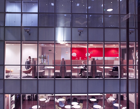 Office interior with red accent wall, showing people working in a modern workspace.