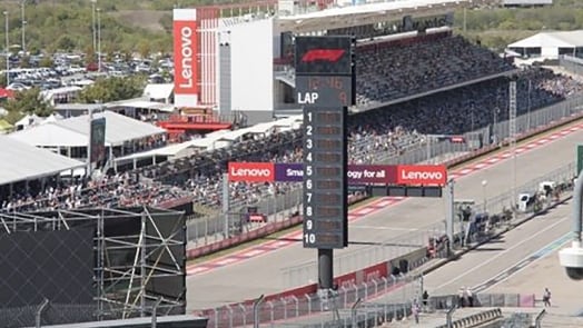 Course avec bannières Lenovo, tableau de pointage et tribune bondée.