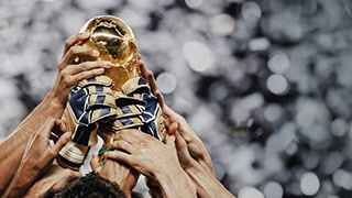 Close-up of multiple football/soccer players' hands holding aloft a FIFA World Cup trophy.