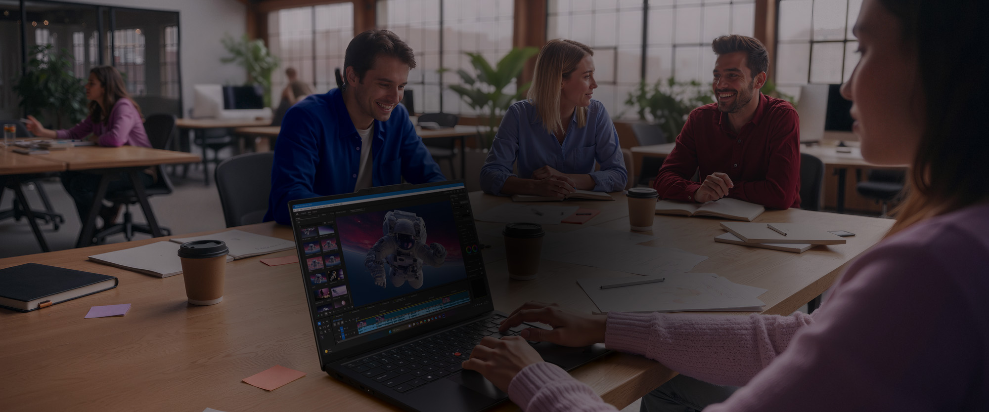 Woman edits 3D graphics on a Lenovo ThinkPad X1 Carbon laptop, as colleagues collaborate at a wooden table.