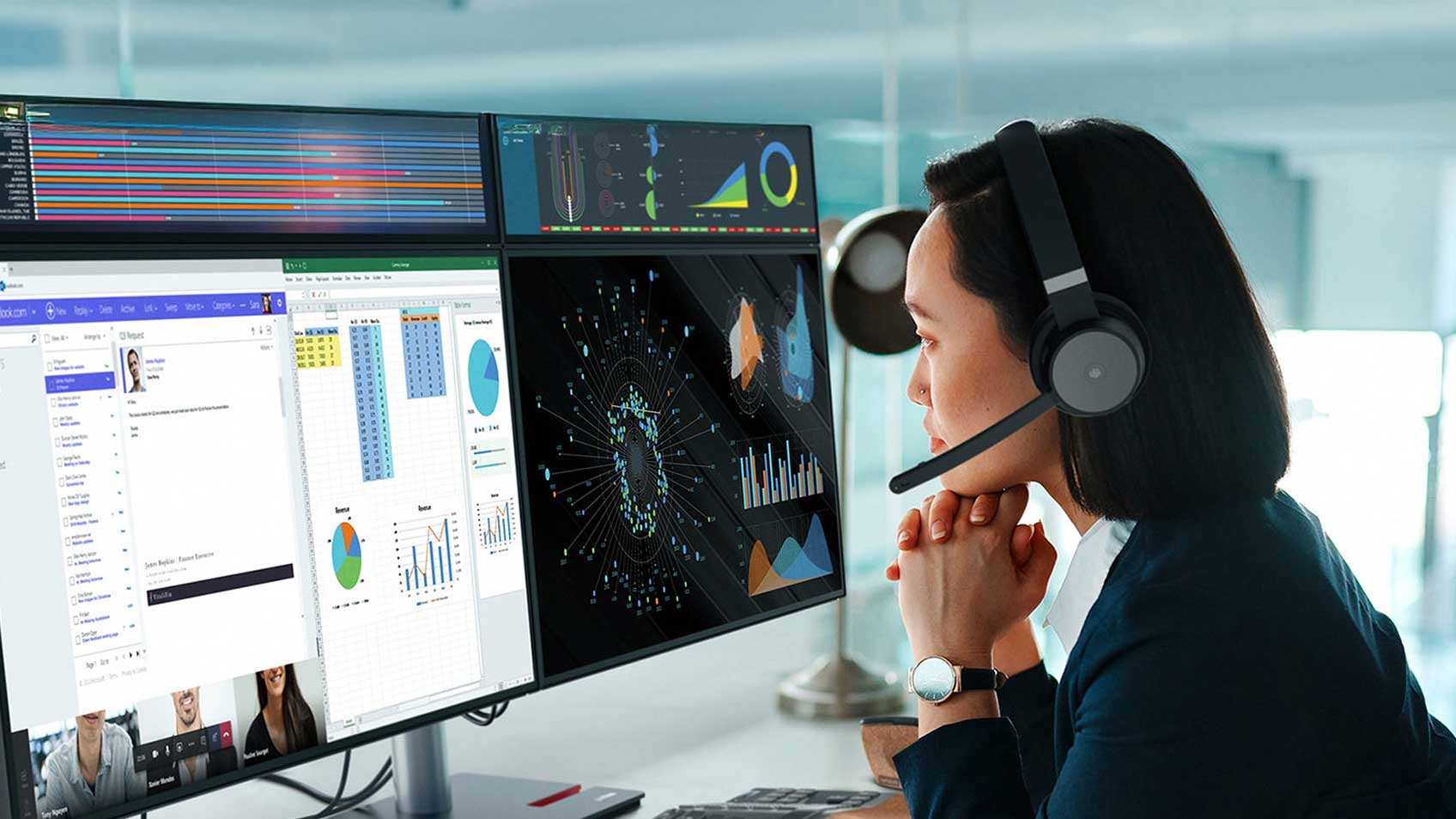 A woman wearing a headset and working at a desk with four monitors 