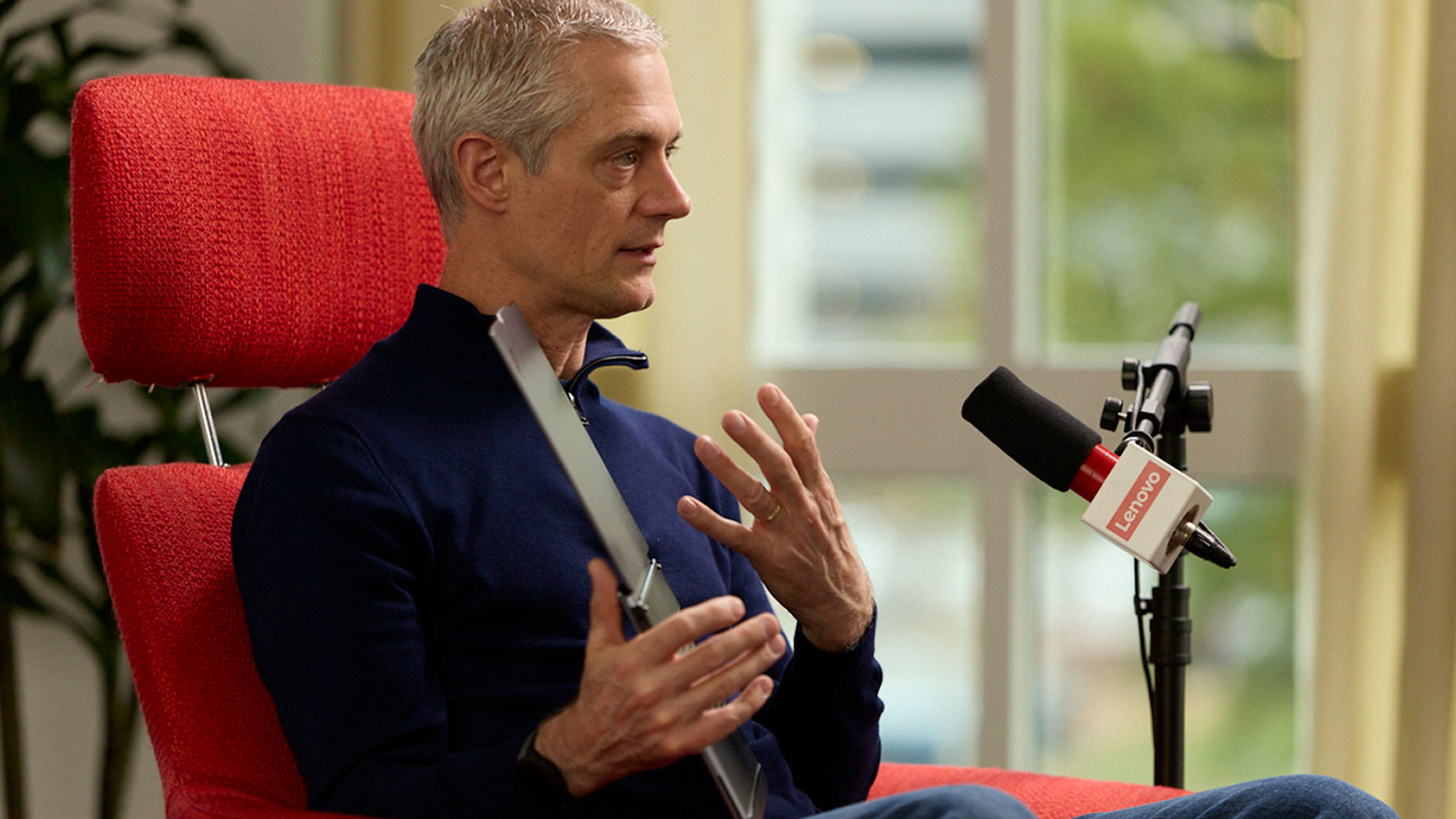 Tom Butler in a red chair speaking into a Lenovo-branded microphone.