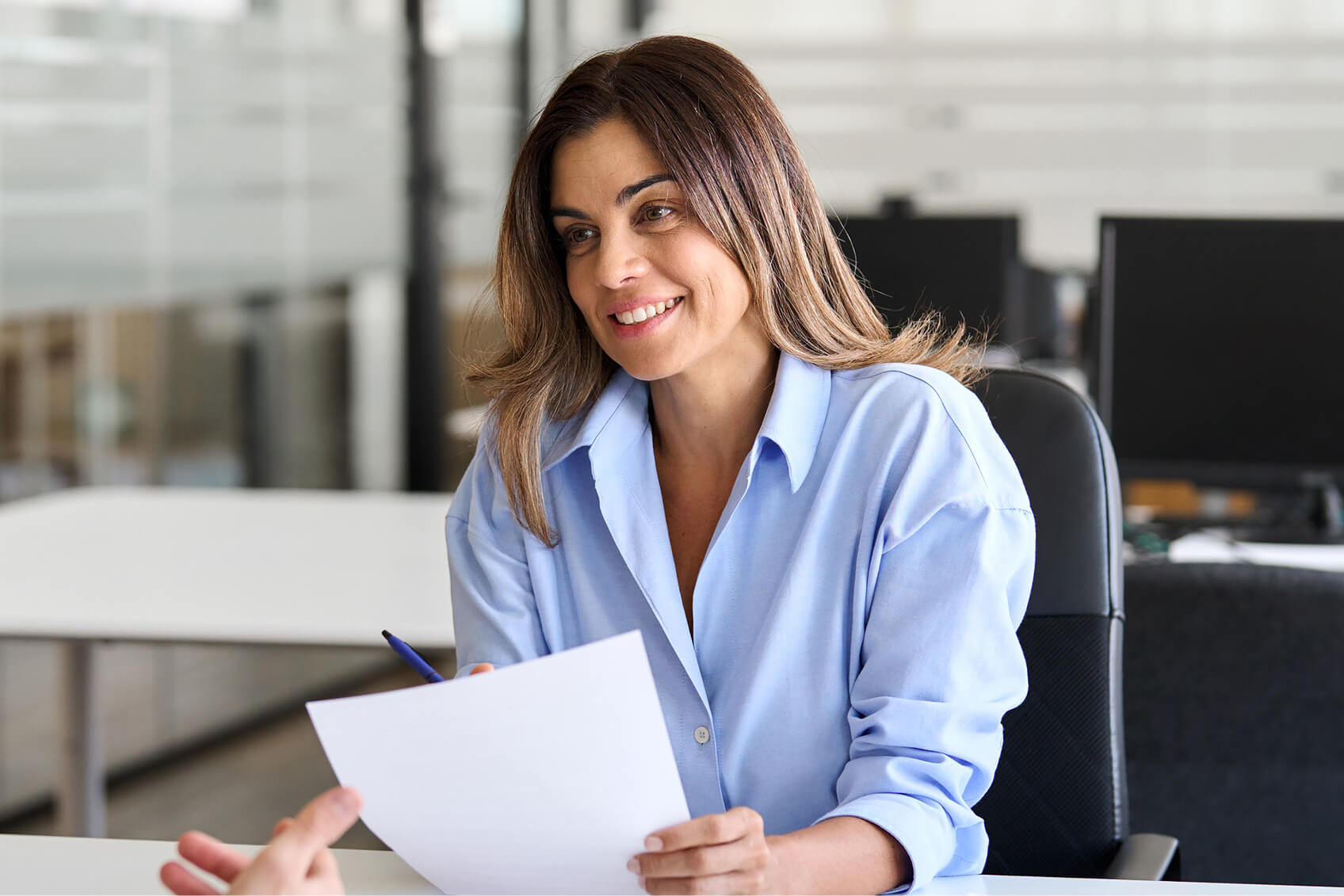 A woman seated at a desk and holding a sheet of paper. 