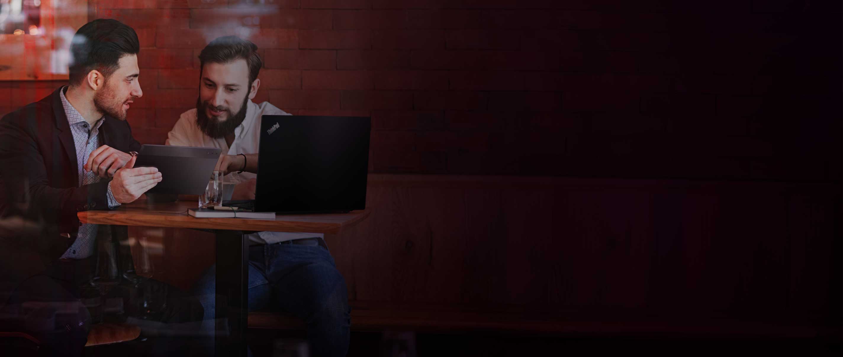 Two men in a coffee shop collaborating on their ThinkPad and tablet.