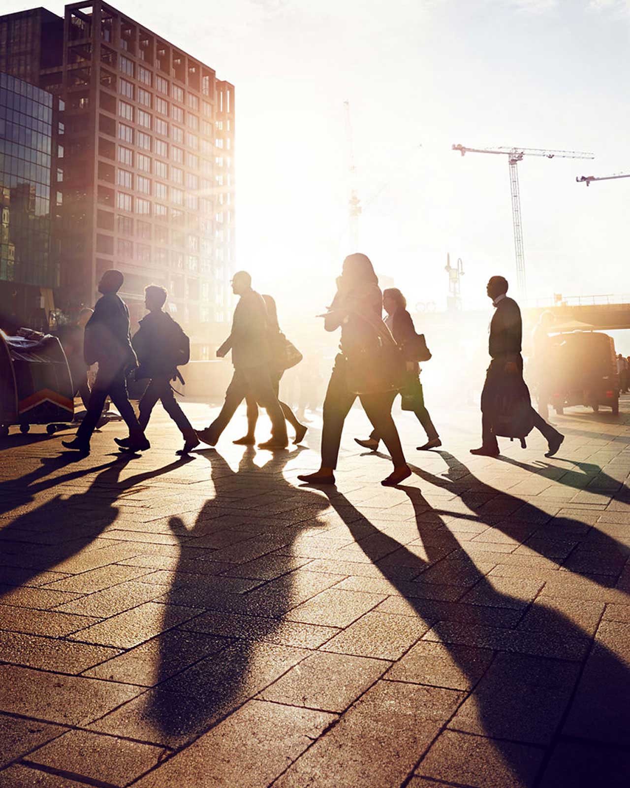 People who are silhouetted by the sun walking to work in the city