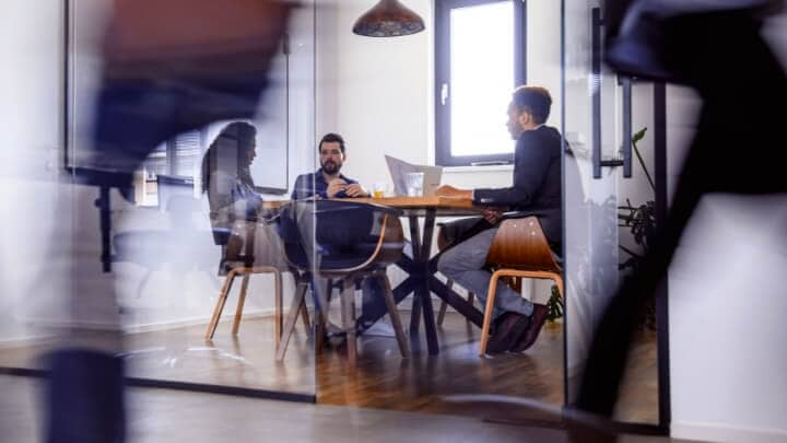 Image of people working inside an office sitting at a table. 