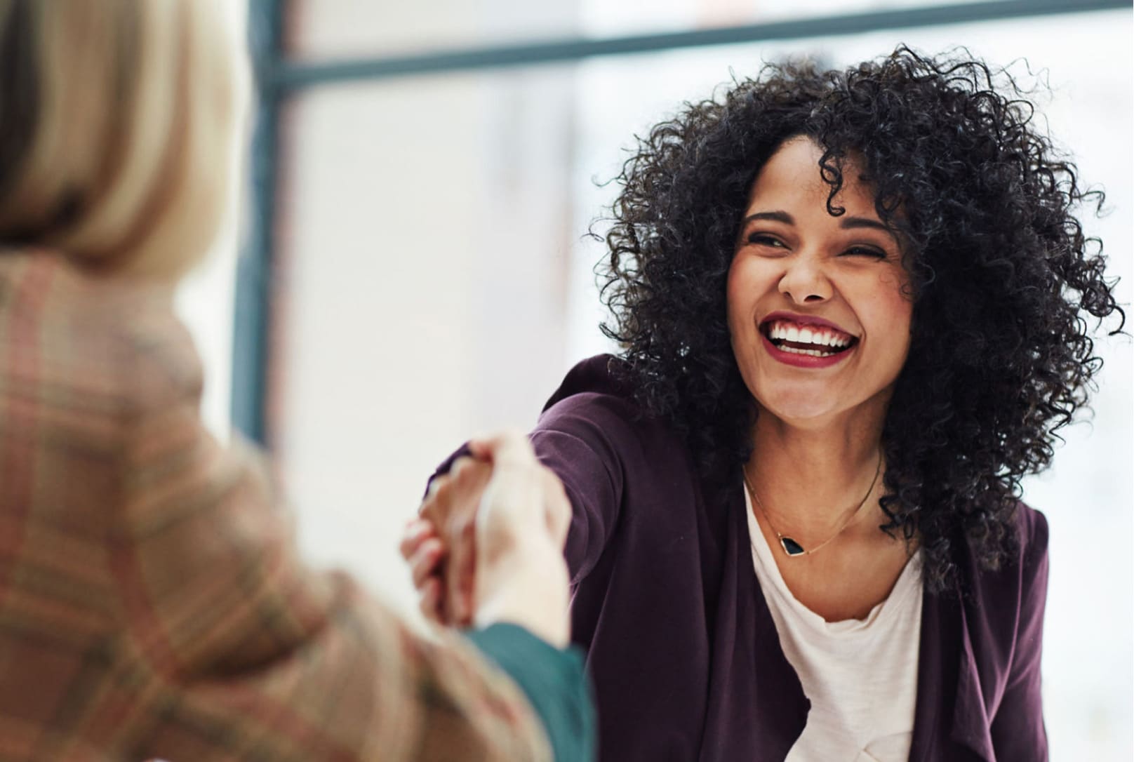 A woman smiling and reaching out to shake someone’s hand