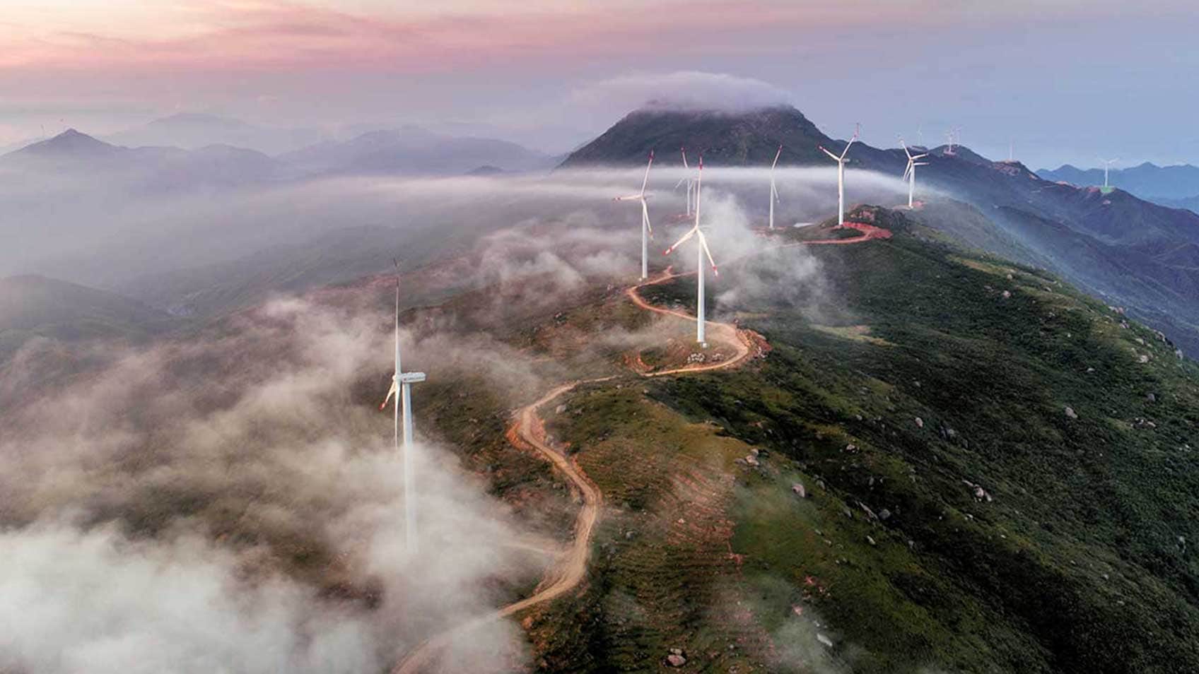 Éoliennes au sommet d’une colline avec une lumière rouge qui tissait entre les deux.