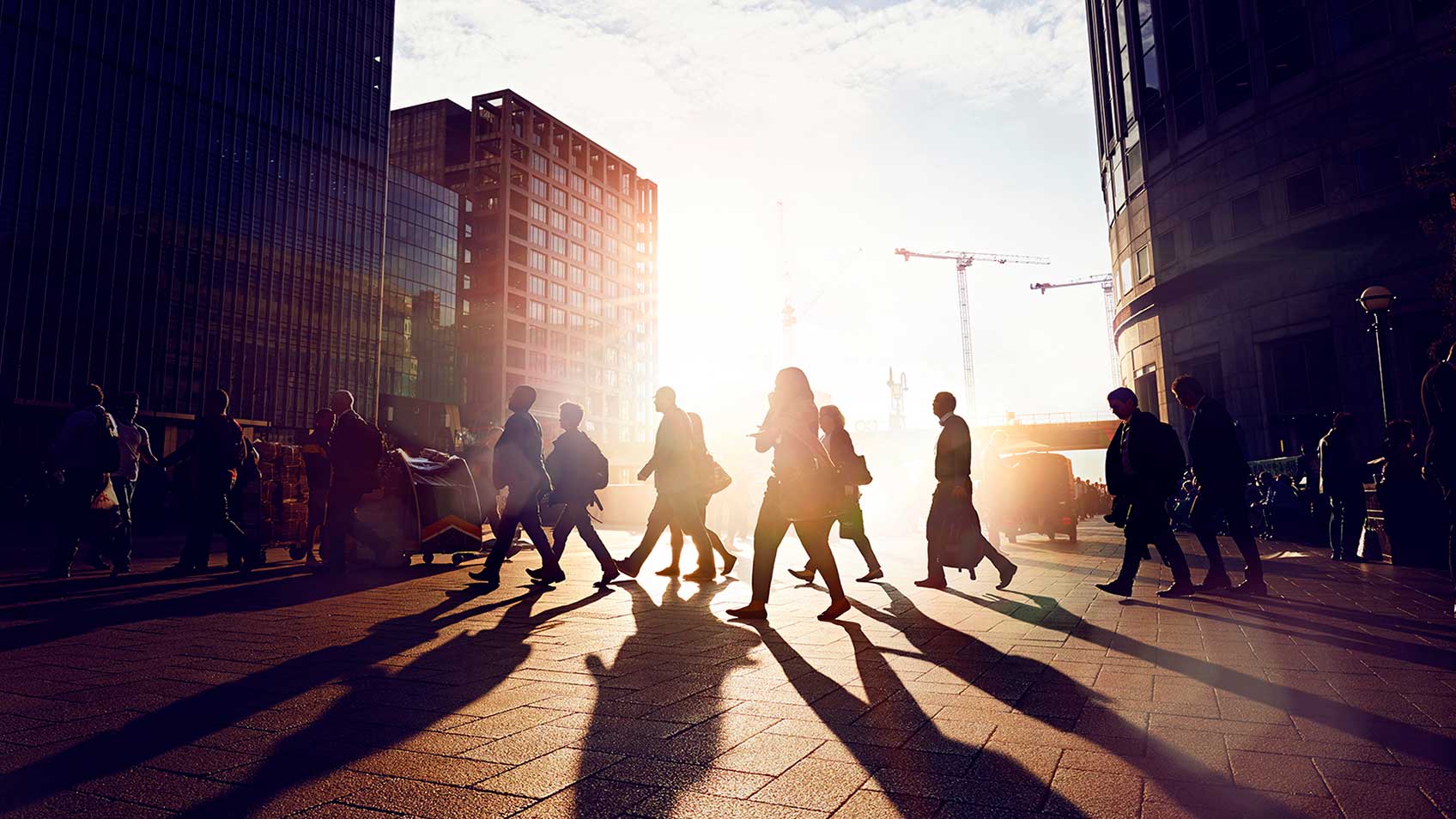 Un groupe de personnes marche à travers la rue tandis que le soleil se couche derrière eux.
