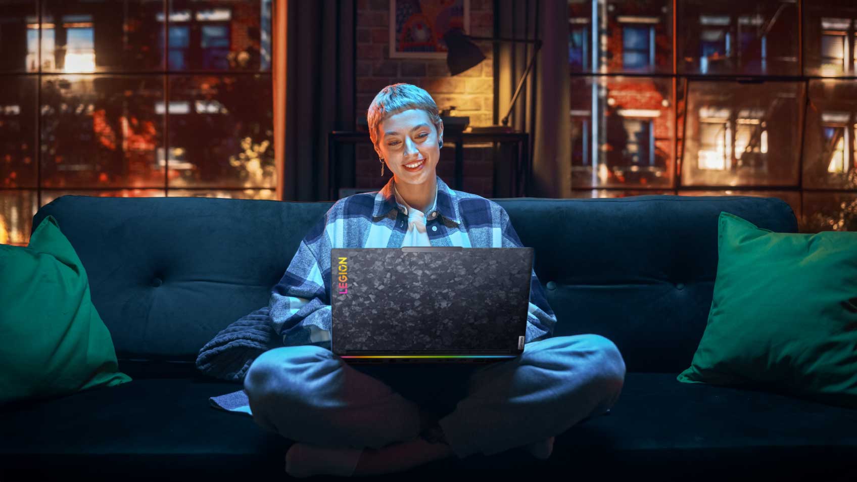 A woman in an urban apartment sitting on a couch and working on her laptop during the evening