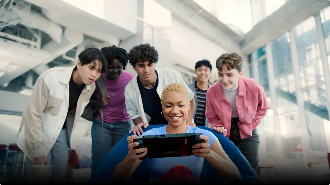 A group of friends standing around one person playing a Legion Go