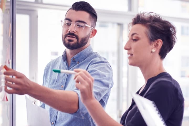 Two professionals collaborating with a marker and board in a bright office setting