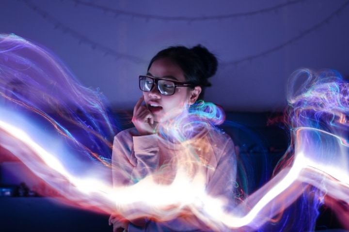 A young woman with glasses sits amid swirling purple and blue light patterns.