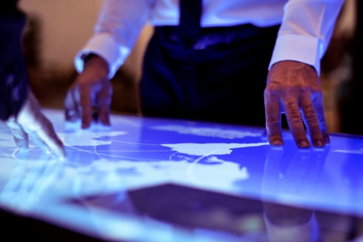 Hands on an illuminated screen displaying a digital map with blue glowing routes.